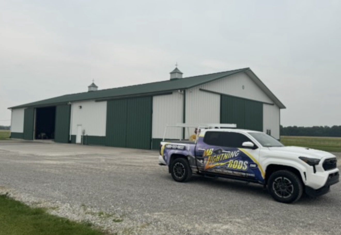 Large green metal pole barn in open farm country fitted with lightning protection